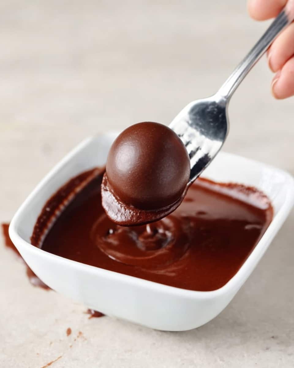 A clear glass bowl filled with several layers of baking ingredients shows chocolate chips piled on the right side, powdered sugar and cocoa powder forming a white and brown layer on top toward the center and left, all resting on a pale yellow mixture at the bottom. A spoon with a silver handle is partly inside the bowl, visible on the right side, resting on the chocolate chips. The bowl is placed on a white marbled surface. photo taken with an iphone --ar 4:5 --v 7