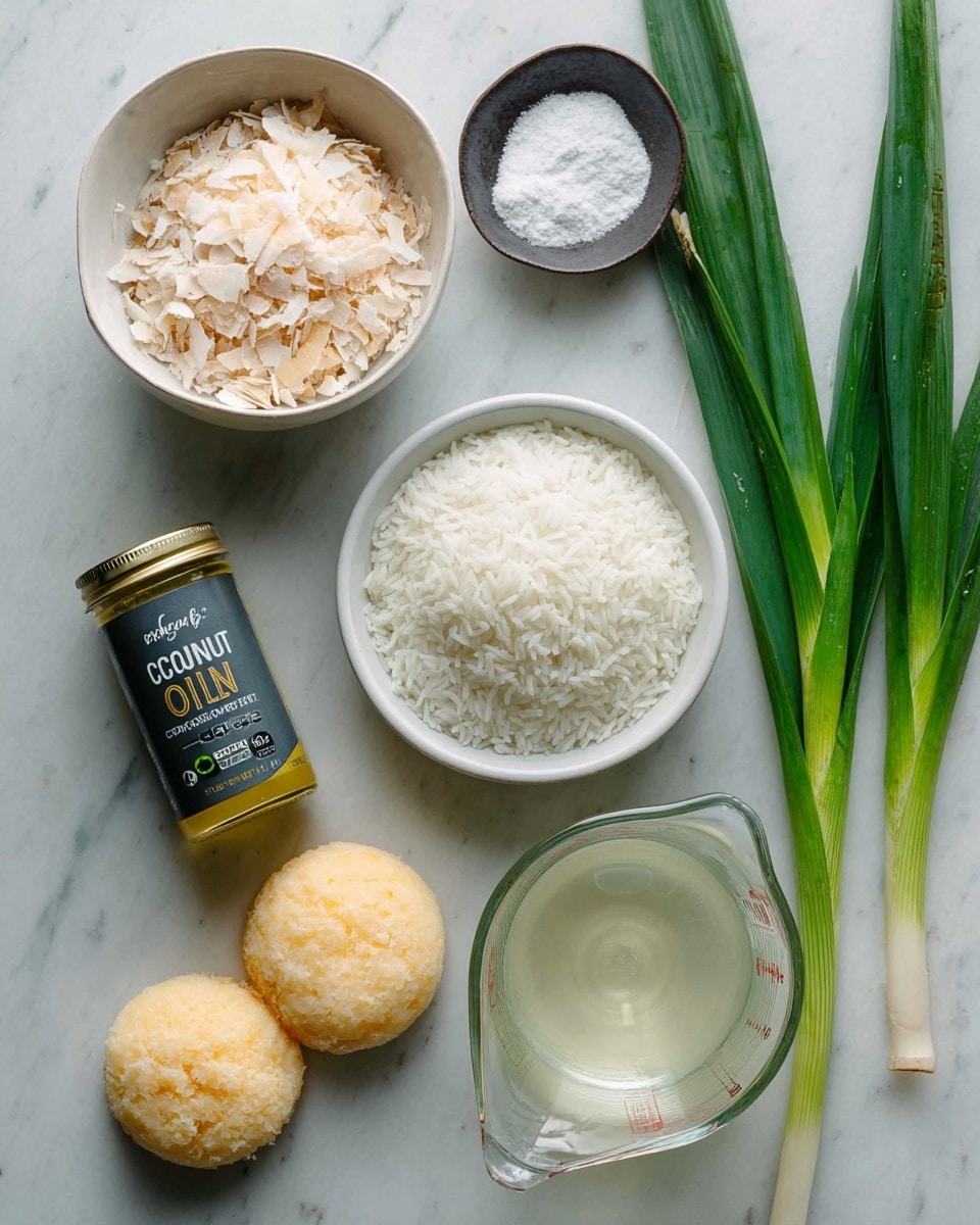 The image shows a white marbled surface with various ingredients arranged neatly. There is a white bowl filled with dry, light beige flakes placed at the top left. Below it is a white bowl containing raw white rice grains. Next to the rice, two round pieces of pale yellow food are placed side by side. Nearby, a small dark dish holds white granulated salt. On the right side, there are green stalks with long leaves. At the bottom, there is a clear measuring cup filled with a creamy white liquid and a glass jar with a yellowish oil labeled