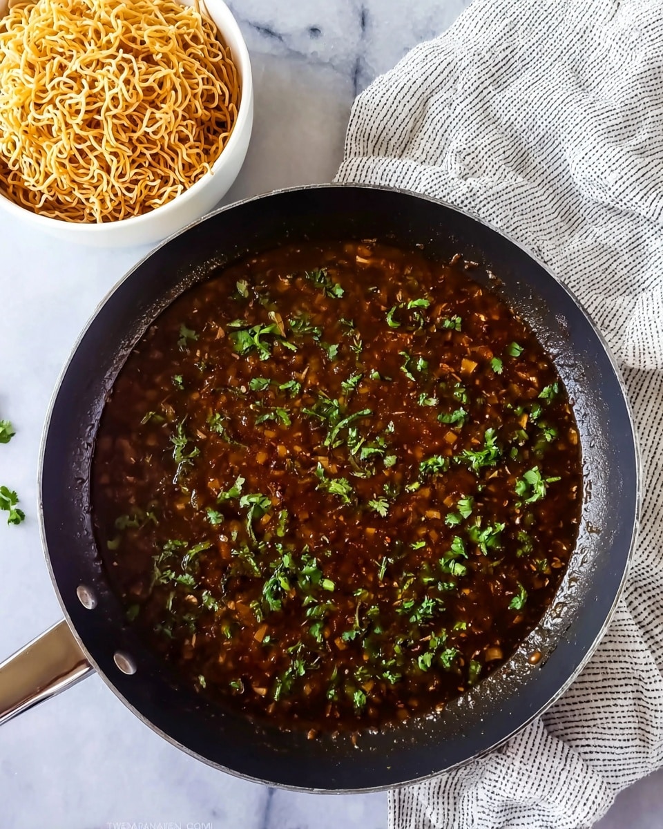 A black pan filled with a dark brown sauce that has small visible pieces of ingredients giving it a textured look, topped with scattered fresh green chopped herbs. To the top left, a white bowl holds a mound of light golden crispy fried noodles with a curly texture. A white cloth with gray stripes is placed in the upper right corner on a white marbled surface. Photo taken with an iphone --ar 4:5 --v 7