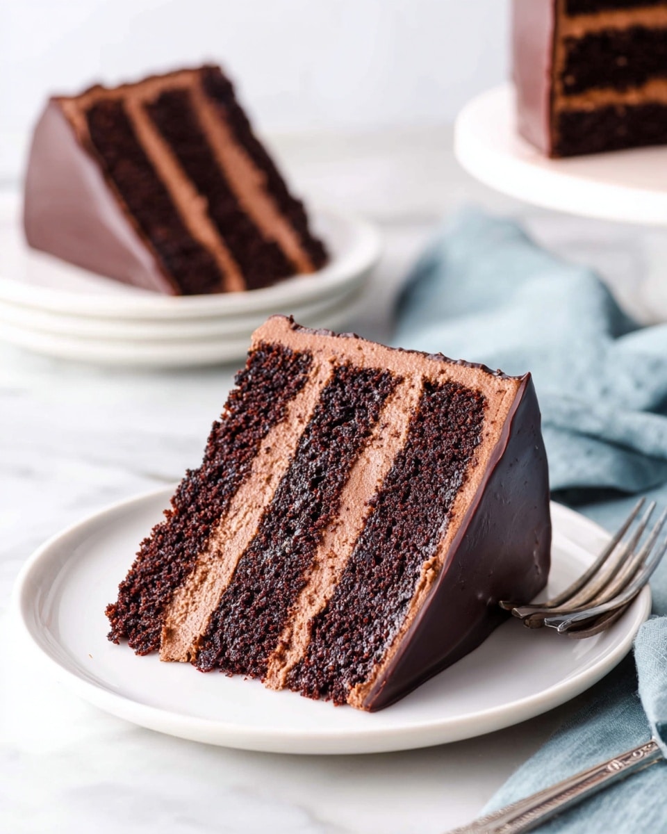 A slice of four-layer dark chocolate cake sits on a white plate on a white marbled surface. The cake has three thick layers of smooth light brown chocolate frosting between each dark, moist chocolate cake layer. The outside edge of the slice is coated in a glossy, dark chocolate ganache. In the background, another slice of the same cake rests on a white plate. A silver fork is placed near the plate, and a soft blue cloth is also seen to the side. Photo taken with an iphone --ar 4:5 --v 7
