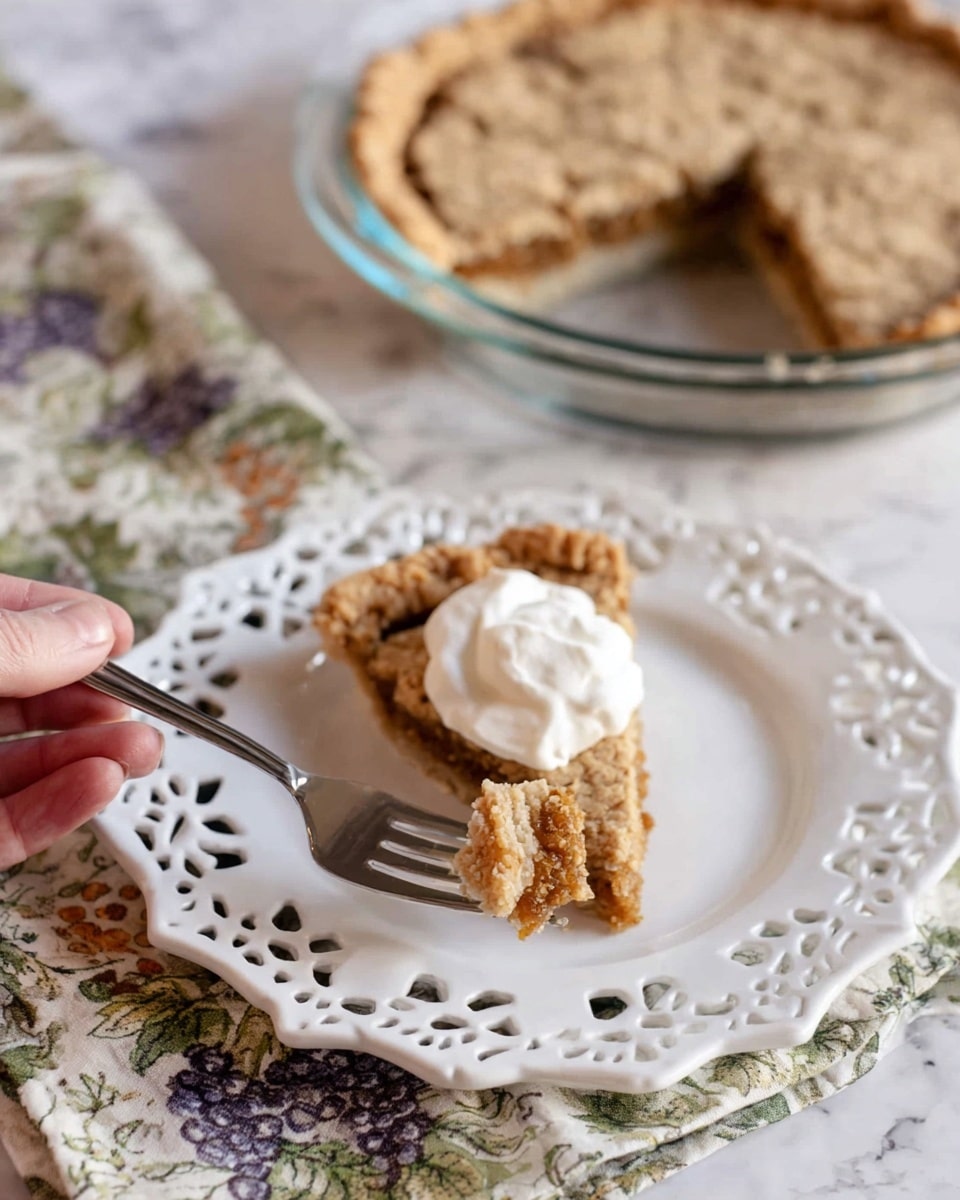 A slice of pie with a light brown cracked crust sits on a white decorative plate with cut-out patterns around the edge. The pie slice has two visible layers: a golden brown crumbly base layer with some texture, and a thin, slightly cracked crust layer on top, topped with a dollop of white whipped cream. A woman's hand holds a silver fork with a small piece of the pie. In the background, a larger clear glass pie dish contains the rest of the pie, showing the same crust and crumb filling, resting on a cloth with a grapevine pattern. The whole scene is set on a white marbled textured surface. photo taken with an iphone --ar 4:5 --v 7