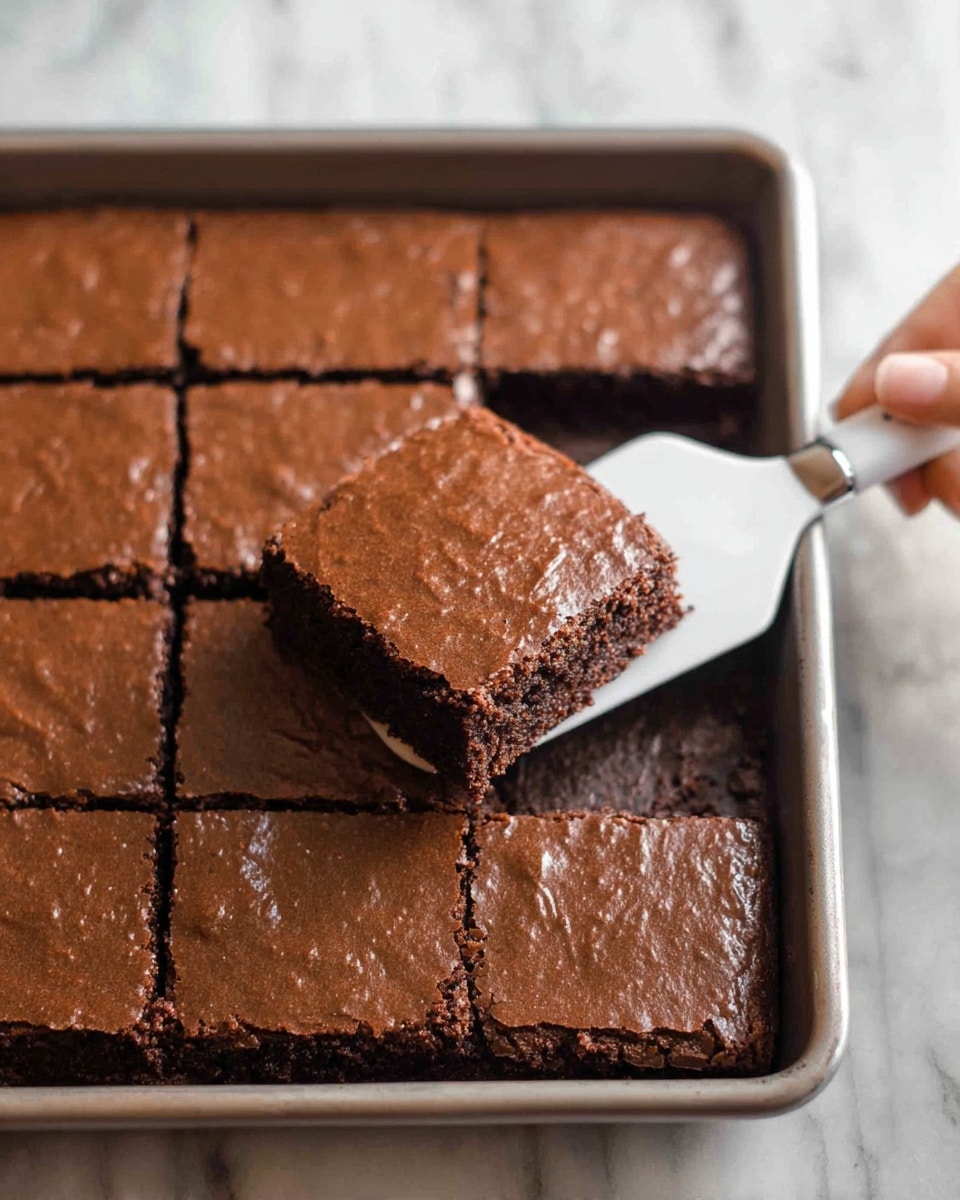 A close-up image shows a square chocolate brownie being lifted from a baking pan with a white-handled spatula held by a woman's hand. The brownie has a smooth, shiny, and slightly cracked top layer in a rich brown color, with a slightly darker, moist interior visible at the edges. The pan is filled with neatly cut squares of the same brownies, all showing the same textured surface and moist baked interior. The pan rests on a white marbled surface. photo taken with an iphone --ar 4:5 --v 7