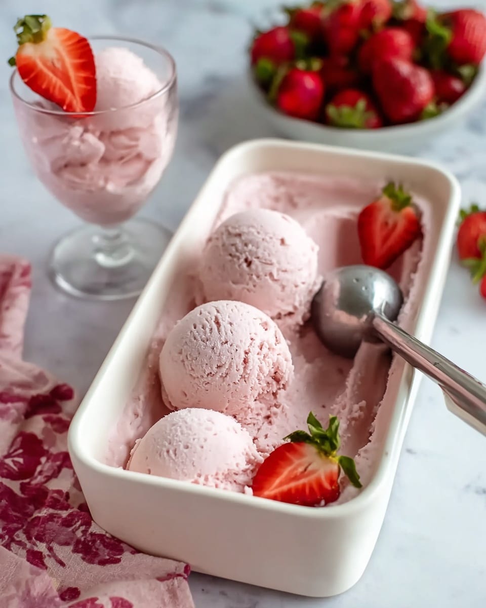 A white container filled with pale pink strawberry ice cream, with three smooth ice cream scoops in the middle and a metal ice cream scoop on the right side. Two red strawberry halves with green leaves are placed on top, one on the left and one near the scoop. In the background, there is a glass cup also filled with the same pink ice cream and topped with two strawberry halves. The scene is set on a white marbled surface with a pink and white cloth under a bowl of whole strawberries. Photo taken with an iphone --ar 4:5 --v 7