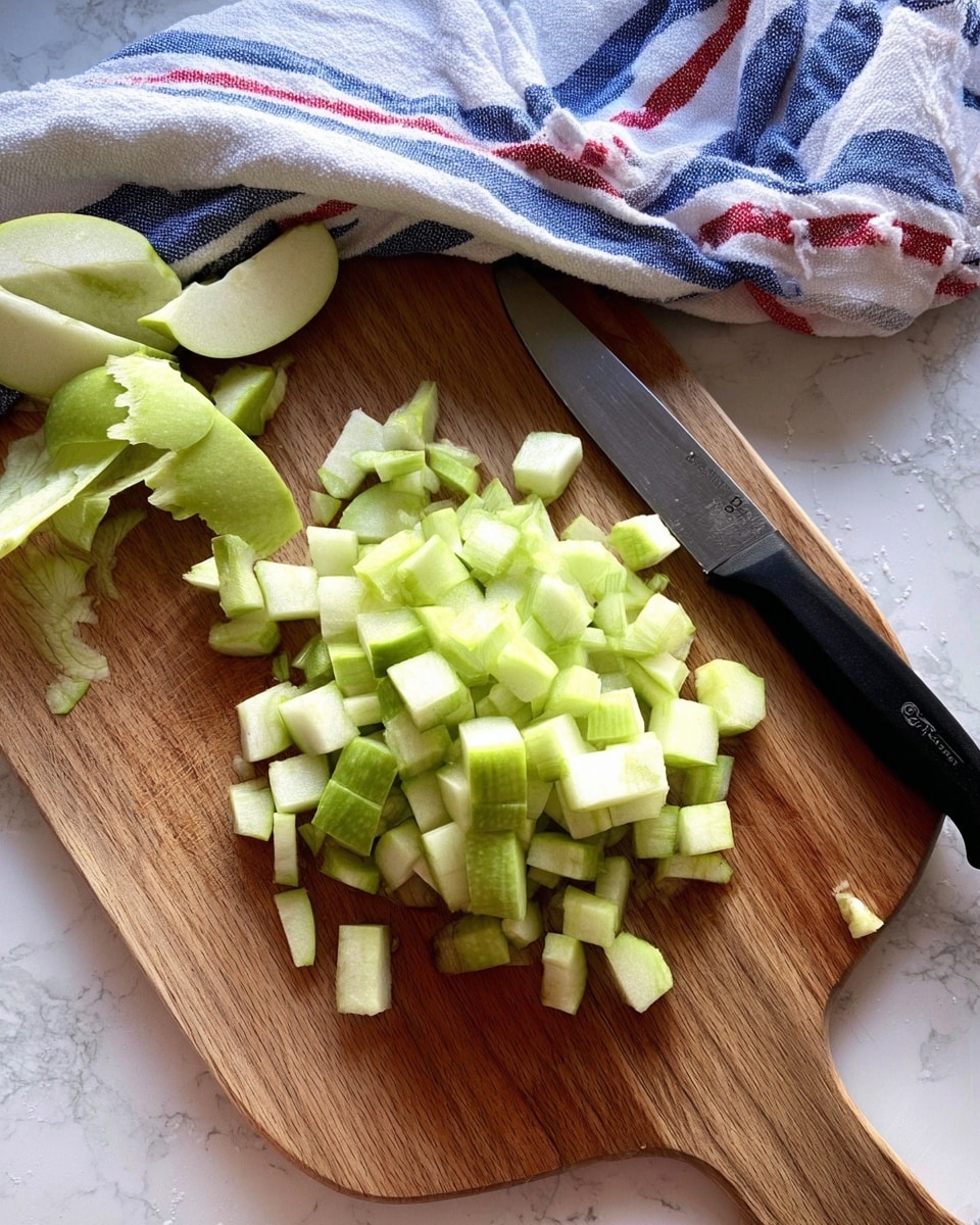 The image shows a wooden cutting board on a white marbled surface with chopped pieces of green apple in the center and peeled green apple skin scraps on the upper left part. On the right side of the board, a black knife rests near the apples. A blue, white, and red striped cloth is casually placed in the background above the cutting board. Photo taken with an iphone --ar 4:5 --v 7