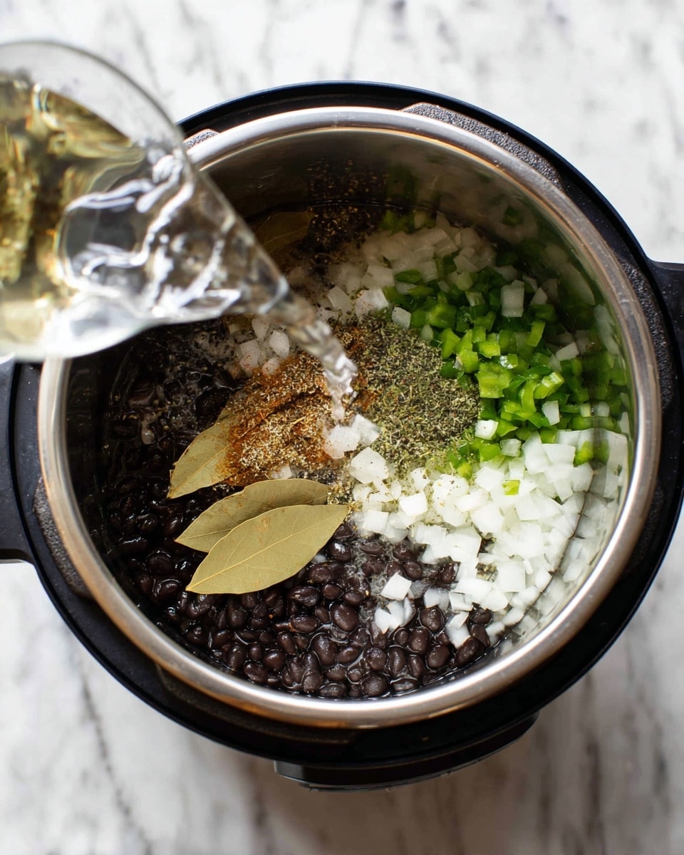 Inside a shiny metal pot, there are four main layers: at the bottom are small black beans, above them are chopped white onions, to the left are small pieces of green peppers, and on top of the beans and onions are two pale brown bay leaves and a sprinkle of light brown and black spices. Water is being poured into the pot from the top left corner. The pot sits on a black appliance base against a white marbled surface. photo taken with an iphone --ar 4:5 --v 7