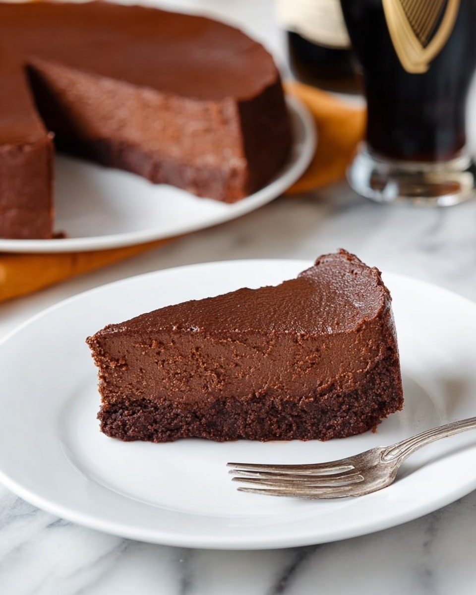The image shows a slice of dark chocolate cake with a smooth and dense texture, placed on a white plate. The cake slice has two clear layers: a thicker bottom layer that looks rich and fudgy, and a slightly lighter, soft top layer with a cracked surface. A small silver fork lies next to the cake on the plate. In the background, there is the rest of the chocolate cake on a transparent glass plate, and partially visible glasses filled with dark liquid. The whole setting rests on a woven brown mat with a white marbled surface under it. The lighting is warm and natural, highlighting the cake’s rich color and moist texture. Photo taken with an iphone --ar 4:5 --v 7