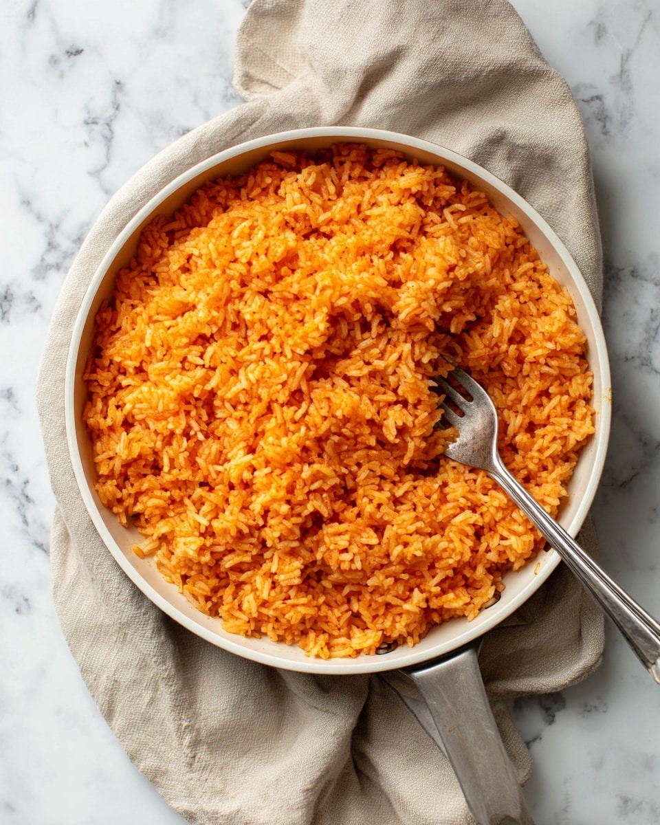 A round white pan filled with orange-colored rice that looks soft and fluffy, with a slightly uneven texture showing the grains separated well. A silver fork rests inside the pan slightly pushed into the rice near the center. The pan sits on a folded beige cloth that is laid on a white marbled surface. The pan has a simple handle on the right side. photo taken with an iphone --ar 4:5 --v 7