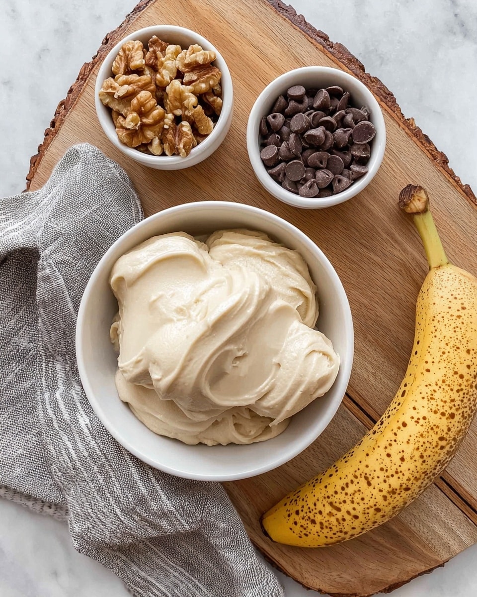A white bowl filled with creamy, smooth beige banana ice cream is placed on a light wood cutting board with a rustic edge. Above it, two small white bowls sit side by side—one contains medium brown walnut halves, and the other is full of dark brown chocolate chips. To the right of the bowls is a whole yellow banana with brown spots, resting on the board. A striped gray and white cloth is folded and laid casually on the left side of the board, all set on a white marbled surface. Photo taken with an iphone --ar 4:5 --v 7