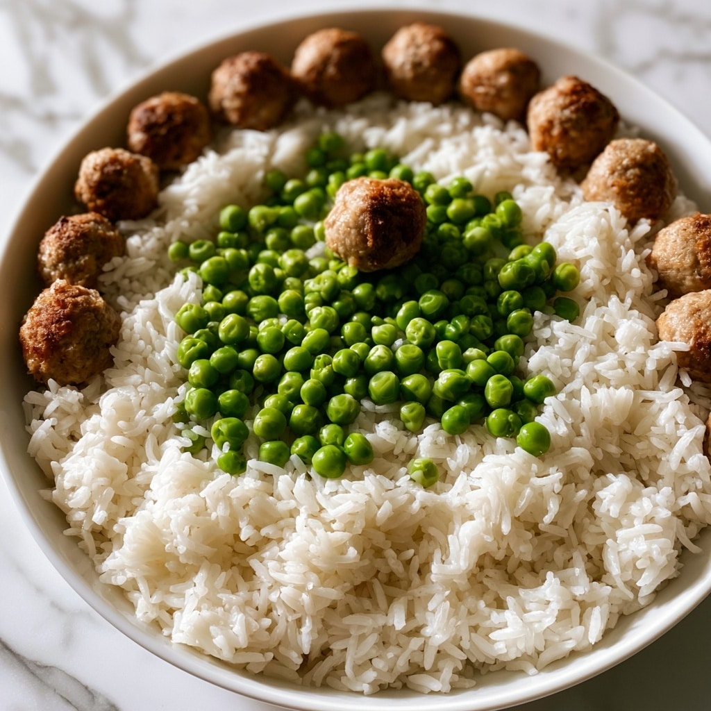 The image shows a close-up of a dish with three layers: a bottom layer of fluffy white rice with individual grains visible, a middle layer of bright green peas scattered unevenly, and a top layer of small brown meatballs with a slightly rough texture, placed mostly around the edge of the dish and some near the center. The dish is in a shallow white bowl on a white marbled surface. The colors are natural and fresh, with a simple and clean composition. Photo taken with an iphone --ar 4:5 --v 7