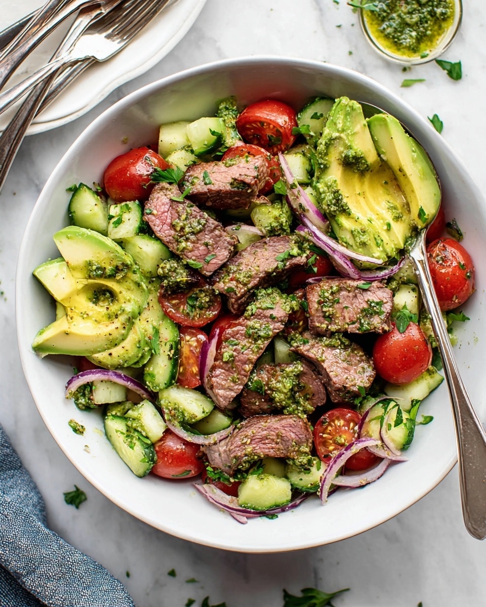 A white bowl holds a fresh salad with several layers; the base layer is chopped green cucumbers and halved red cherry tomatoes, mixed with thin slices of purple-red onion. On top, slices of bright green avocado are placed evenly around the bowl. Large chunks of cooked steak with browned edges and pink centers are scattered on top. The whole dish is drizzled with a green herb pesto sauce, adding a textured and vibrant finish. A silver spoon rests inside the bowl. The white marbled surface beneath the bowl shows some loose parsley leaves and a white plate with metal forks. photo taken with an iphone --ar 4:5 --v 7