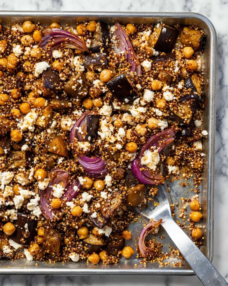 The dish shows a large metal baking tray filled with a mix of roasted eggplant chunks that are dark purple and brown, golden brown chickpeas, small white crumbles of cheese, light tan quinoa mixed with black quinoa seeds, and scattered slices of roasted red onion in reddish-purple hues. The textures range from soft cooked eggplant, slightly crispy quinoa, to firm chickpeas, all evenly mixed together. A metal spatula with a gray handle is placed on the bottom right corner, partially under the food. The tray rests on a white marbled surface. Photo taken with an iphone --ar 4:5 --v 7