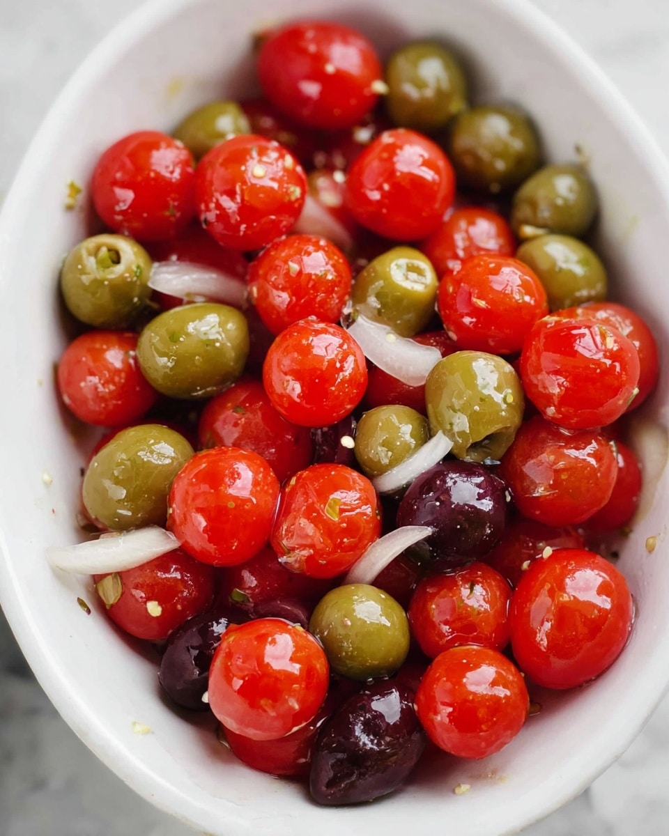 The image shows a close-up of a white bowl filled with a fresh mix of bright red cherry tomatoes and glossy green and dark purple olives. There are thin white slices of onion scattered among the tomatoes and olives. The ingredients are shiny, likely from a light coating of oil or dressing, giving a fresh and juicy look. The bowl is on a white marbled surface. photo taken with an iphone --ar 4:5 --v 7