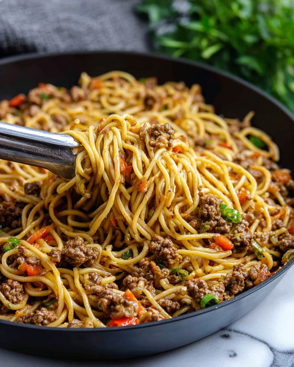 A close-up view of a black pan filled with cooked yellow noodles mixed with small chunks of cooked brown ground meat and small pieces of orange-red and green vegetables spread evenly throughout. Silver tongs hold a portion of the noodles and meat, showing the texture of the soft noodles intertwined with the slightly rough meat pieces and colorful vegetables, all glistening lightly as if freshly cooked, with a blurred green plant in the background and a white marbled surface below. Photo taken with an iphone --ar 4:5 --v 7