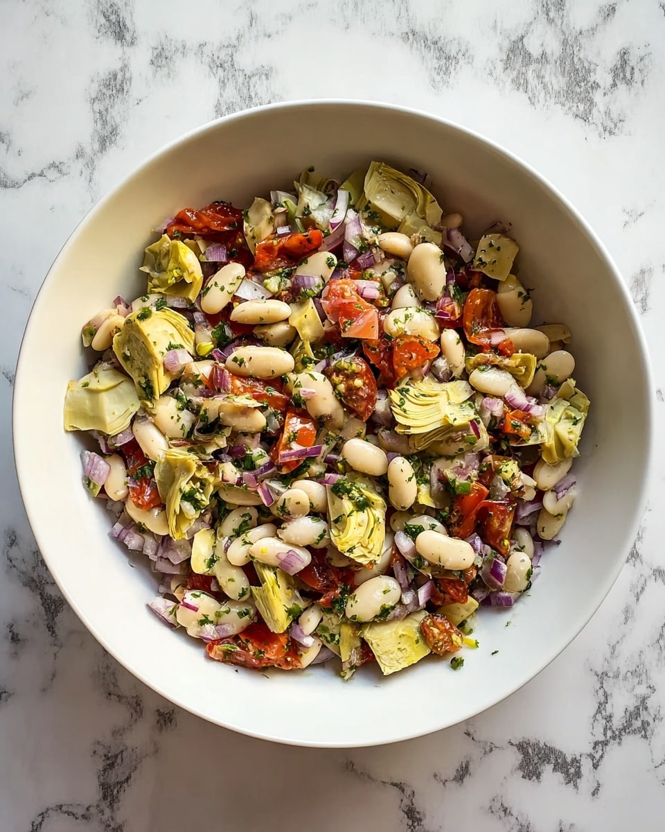 The image shows a white bowl filled with a colorful salad on a white marbled surface. The salad has several layers: the base is made of white beans mixed with small pieces of diced red onion; on top of this are chunks of light green artichoke hearts and small pieces of red tomato; sprinkled throughout are finely chopped green herbs, giving the salad a fresh look. The textures mix the soft beans with the slightly crunchy vegetables, all tossed together lightly. photo taken with an iphone --ar 4:5 --v 7