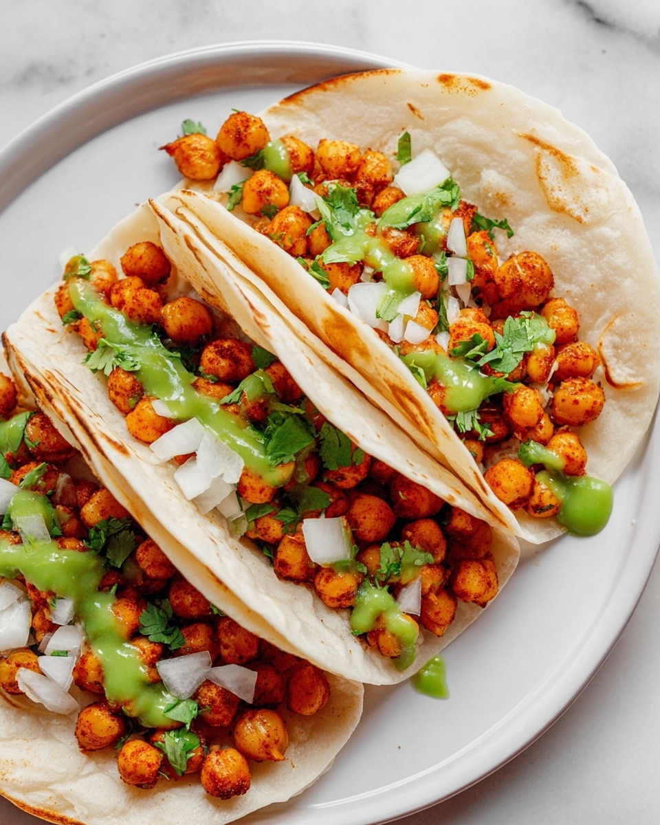 Three soft white tortillas are folded and placed close together on a round white plate. Each tortilla holds a layer of small, cooked chickpeas with a reddish-brown seasoning, topped with chopped white onion, bits of fresh green cilantro, and drizzles of bright green sauce. The chickpeas look slightly crispy, and the tortillas have some light brown spots from cooking. The plate sits on a white marbled surface. photo taken with an iphone --ar 4:5 --v 7