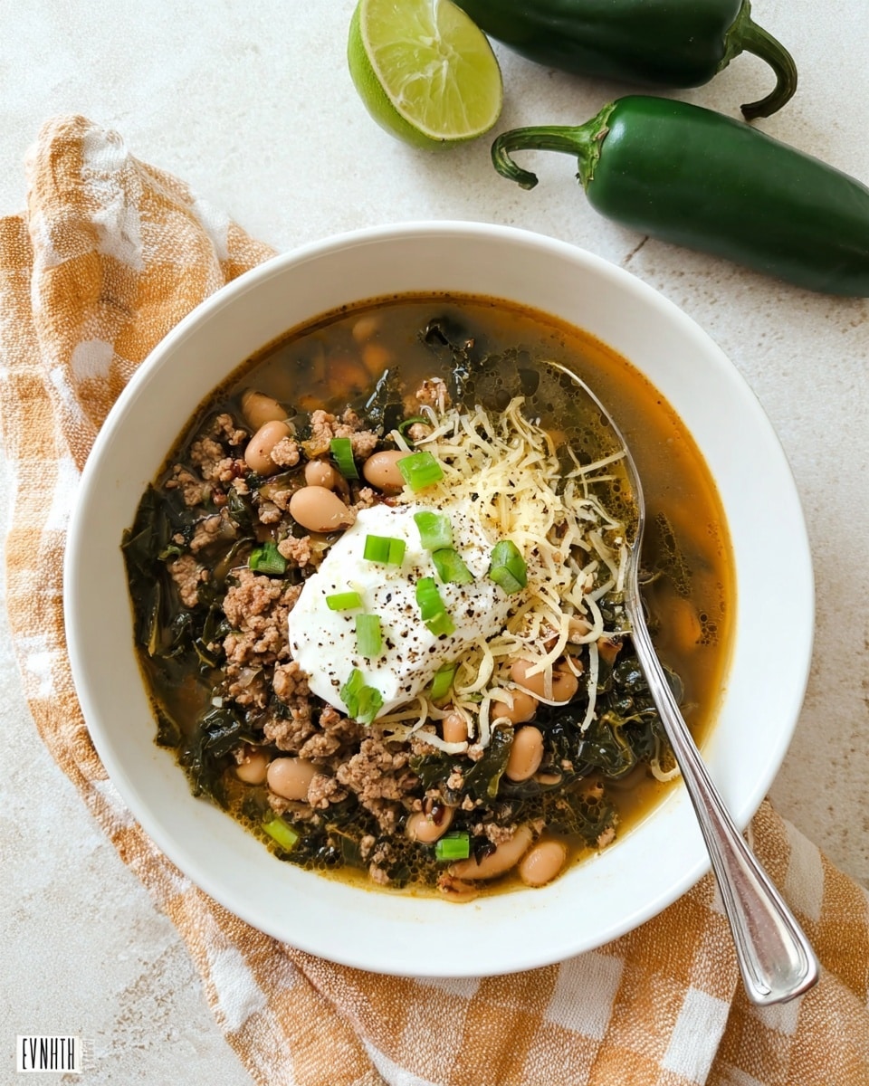 A white bowl on a white marbled textured surface holds a layered soup with a rich broth base, filled with light brown cooked ground meat and pale beige black-eyed peas mixed with dark green leafy vegetables. The soup is topped with a dollop of white sour cream sprinkled with black pepper, thin bright green sliced scallions scattered on top, and finely shredded pale yellow cheese. A silver spoon is placed inside the bowl on the right side. Nearby are a wedge of light green lime and two whole dark green poblano peppers resting on a beige and orange checkered cloth. photo taken with an iphone --ar 4:5 --v 7