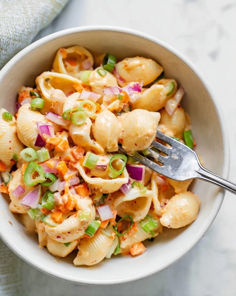 A close-up of a white bowl filled with three layers of food: the first layer is creamy shell pasta in a light orange sauce with a smooth texture; the second layer includes small diced vegetables like orange carrots, green celery, and white onions, scattered evenly; the third layer has thin slices of red onion and green spring onions mixed throughout. A metal fork holds a few shells and pieces of vegetables near the center. The bowl is set on a white marbled surface. photo taken with an iphone --ar 4:5 --v 7