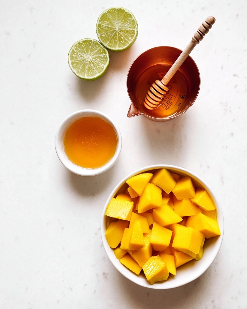 The image shows a white bowl filled with bright yellow mango chunks at the bottom right. Above the bowl is a copper measuring cup with an orange liquid inside. Above the measuring cup is a small white bowl with golden honey and a wooden honey dipper resting on top. At the top left, there are two halves of greenish-yellow lime. The whole setup is placed on a white marbled surface. photo taken with an iphone --ar 4:5 --v 7
