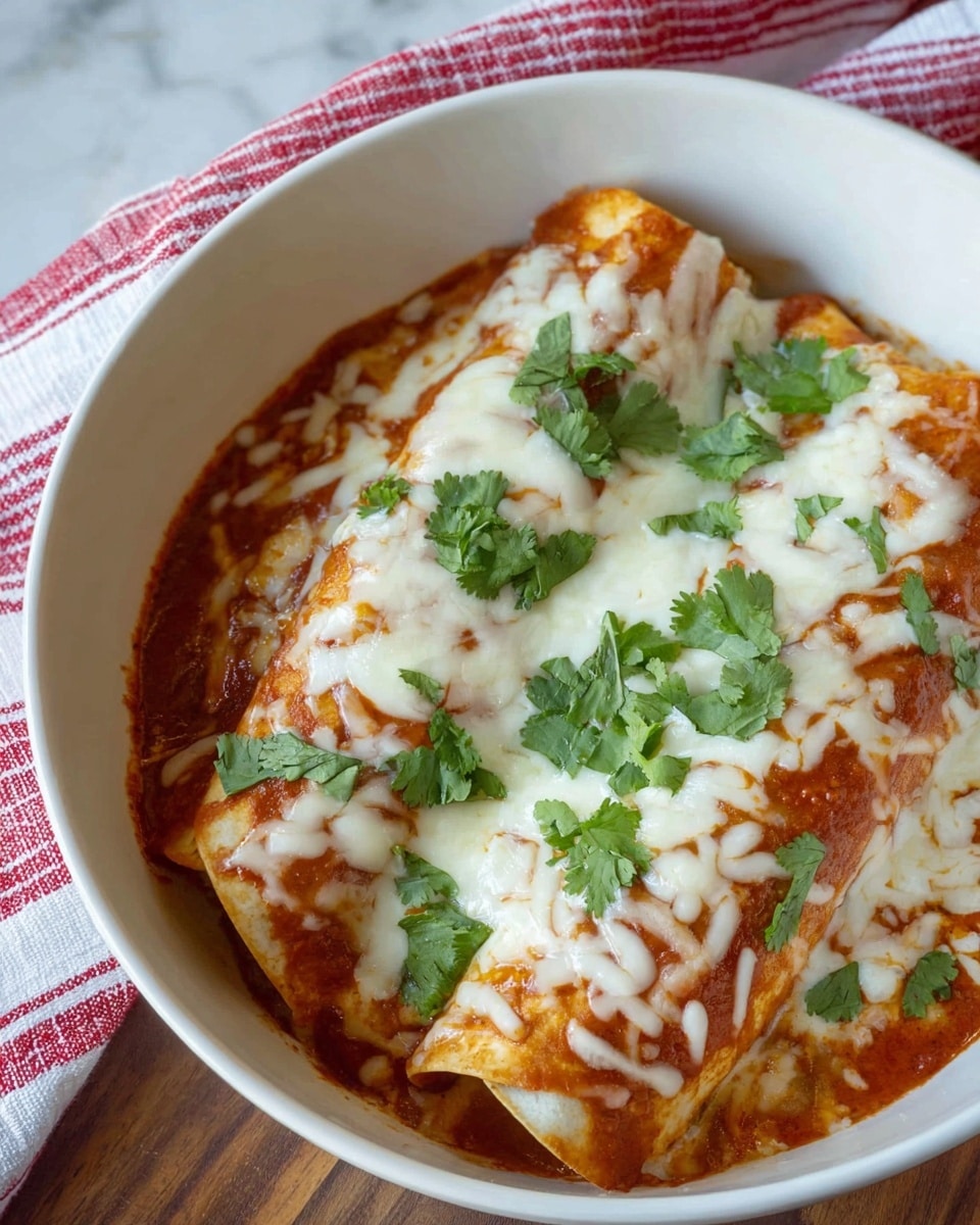The image shows a white bowl filled with two rolled tortillas covered in a red sauce, giving an orange-red base layer. On top, there is a thick layer of melted white cheese with light brown spots, spread evenly over the tortillas. Fresh green cilantro leaves are scattered across the cheese, providing a bright contrast. The bowl is placed on a wooden surface with a white marbled background and a red and white striped cloth partially visible in the upper left corner. The photo taken with an iphone --ar 4:5 --v 7