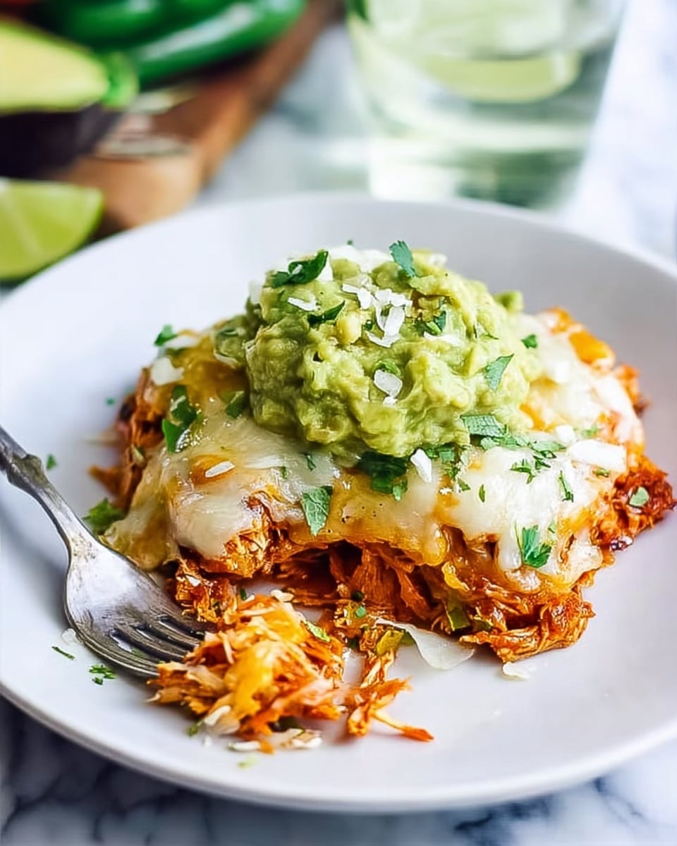 A white plate holds a layered dish with a base of shredded orange chicken mixed with sauce, topped by melted white cheese that looks soft and creamy. On top, there is a large spoonful of light green guacamole sprinkled with small green herb pieces and crunchy bits. A silver fork with some guacamole on its tines rests on the plate, near the food. The plate is placed on a white marbled surface with some blurred green vegetables and a clear glass of water in the background. photo taken with an iphone --ar 4:5 --v 7
