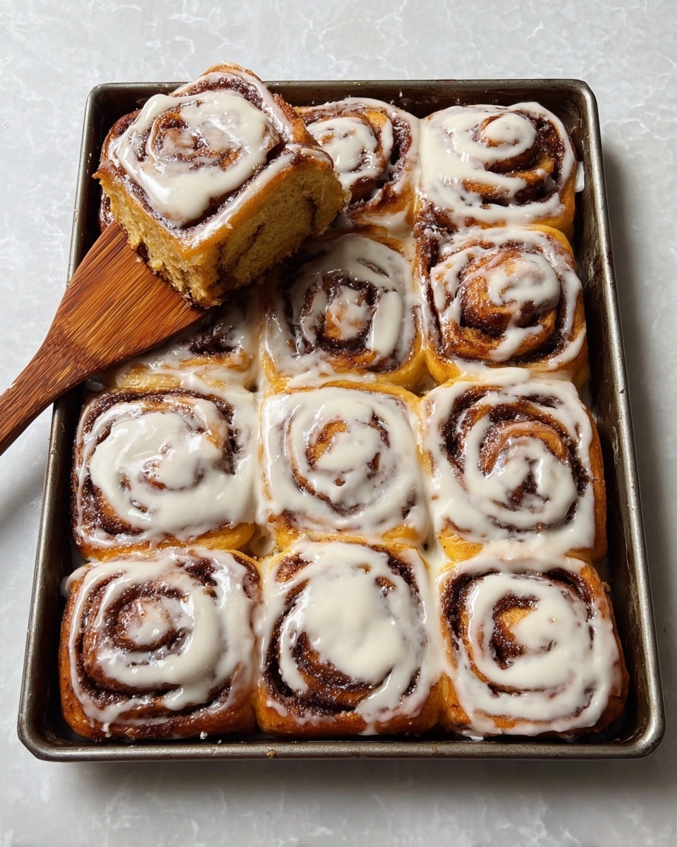 A full baking tray holds nine cinnamon rolls with a light golden brown base and dark brown spiral lines of cinnamon filling. Each roll is topped with a glossy white icing, unevenly spread in a swirl pattern that follows the roll shape. One cinnamon roll is being lifted out with a wooden spatula, showing its soft, fluffy texture and distinct cinnamon swirl inside. The tray rests on a white marbled surface, and the background is softly blurred. photo taken with an iphone --ar 4:5 --v 7