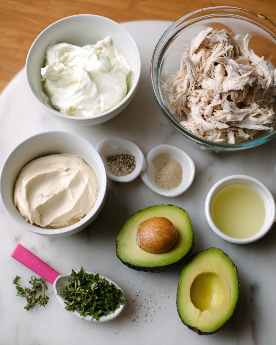 The image shows a wooden table with several white dishes and bowls placed on a white marbled surface. In the center, there is a clear glass measuring cup filled with shredded light brown cooked chicken. To the left, a white bowl holds a fluffy white creamy substance. Below that, another white bowl contains a beige creamy material. In front of these, two halves of a dark green avocado with light green flesh and a seed are positioned close together, with a small bunch of chopped green herbs next to them on a pink measuring spoon. On the upper right, two small white bowls hold a pale yellow liquid and a small pile of black pepper and salt. The whole setup appears orderly on the white marbled texture. photo taken with an iphone --ar 4:5 --v 7