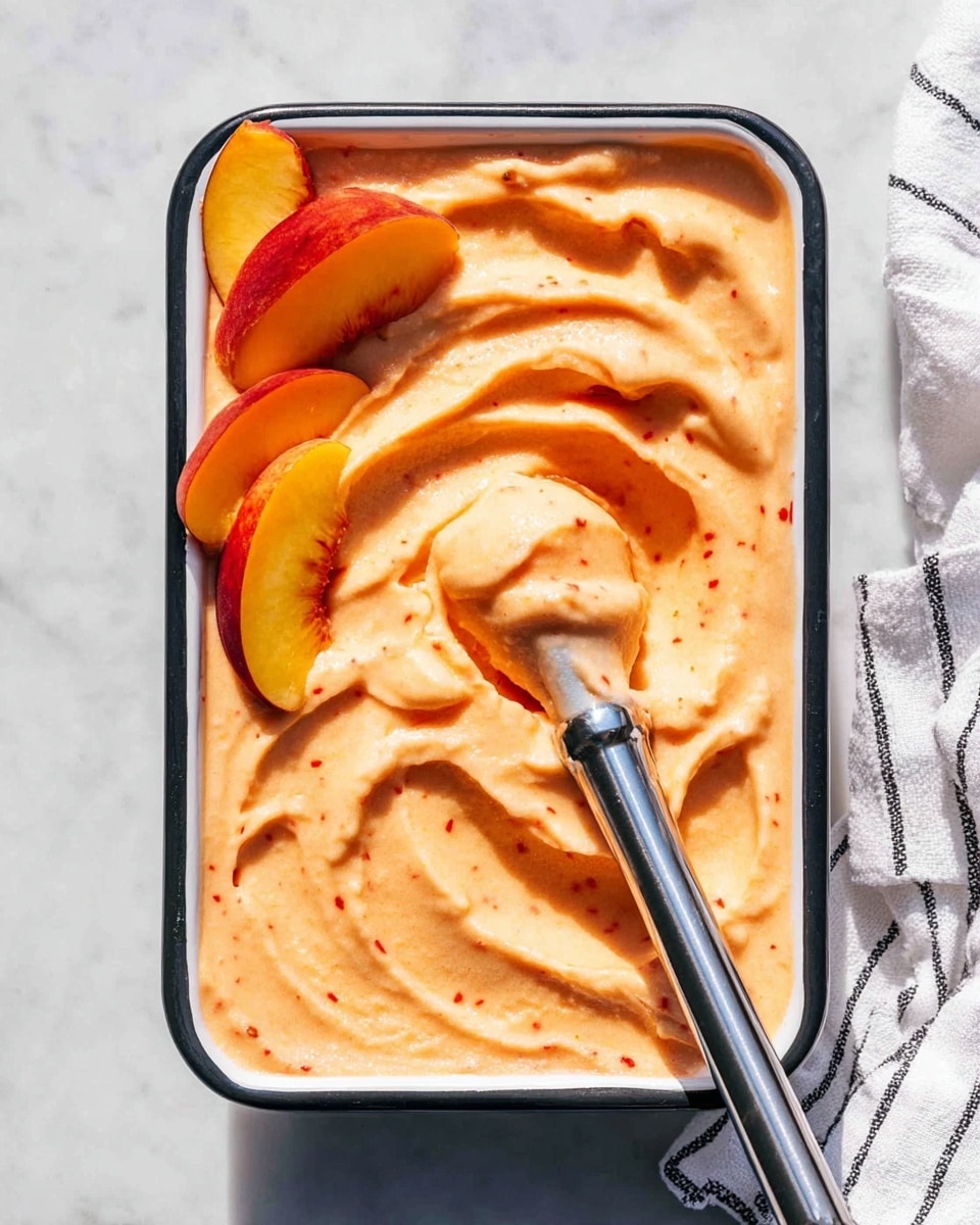 A rectangular white dish with a black rim is filled with smooth, creamy peach-colored frozen dessert with tiny red specks evenly spread throughout. The surface shows soft, swirled peaks and waves. An immersion blender with a shiny silver metal shaft is inserted into the dessert, scooping up a few slices of fresh peach with bright yellow and red skin, partially submerged on the left side. The dish is placed on a white marbled surface, with a white and black striped cloth partially visible on the right side. Photo taken with an iphone --ar 4:5 --v 7