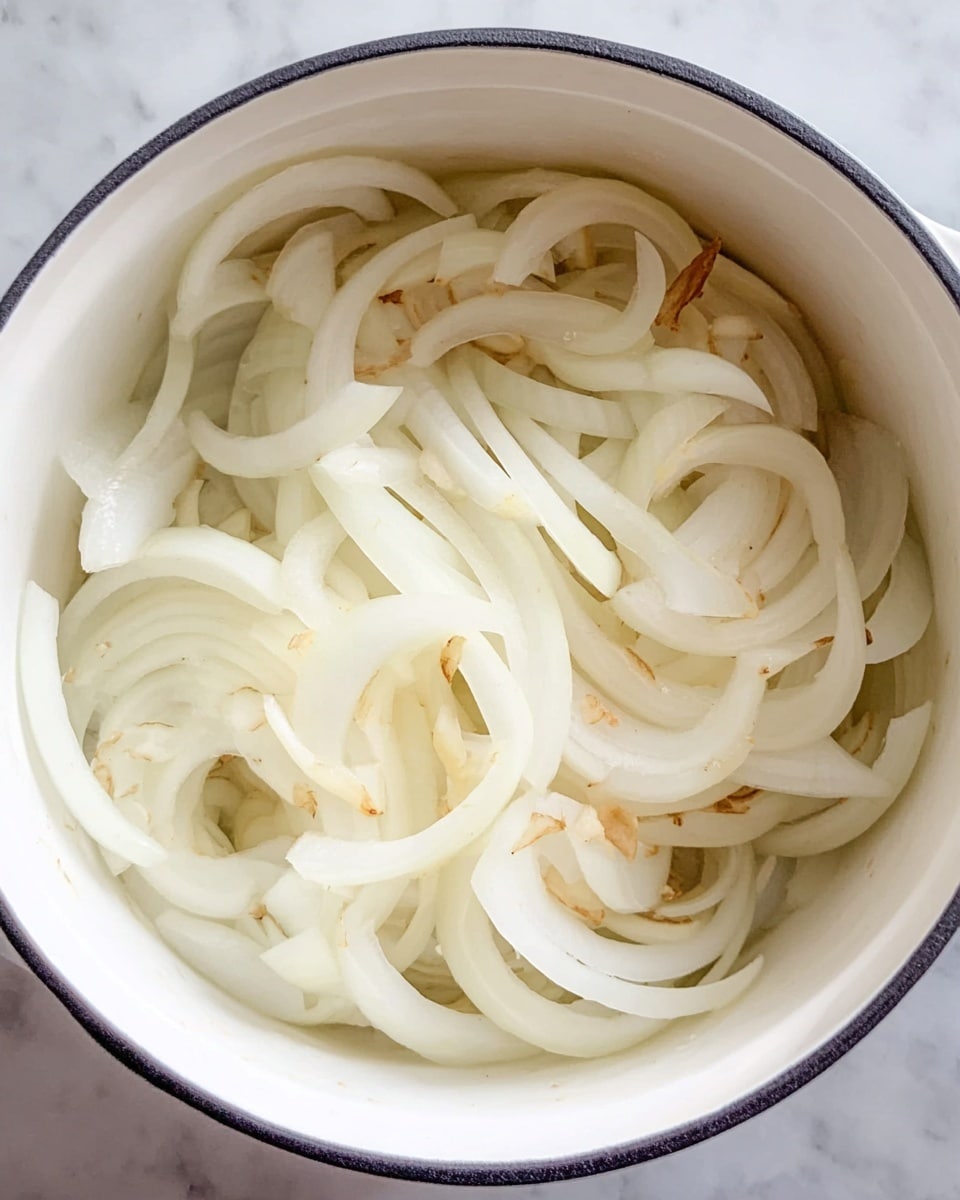 A white pot filled with one layer of sliced white onions. The slices vary in thickness and shape, creating a mix of long curved strips and shorter pieces, some showing light brown edges. The pot is placed on a white marbled surface. photo taken with an iphone --ar 4:5 --v 7
